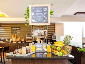 Una barra de desayuno con una pizarra de menú, frascos de condimentos, un cuenco de frutas y un dispensador de jugo.