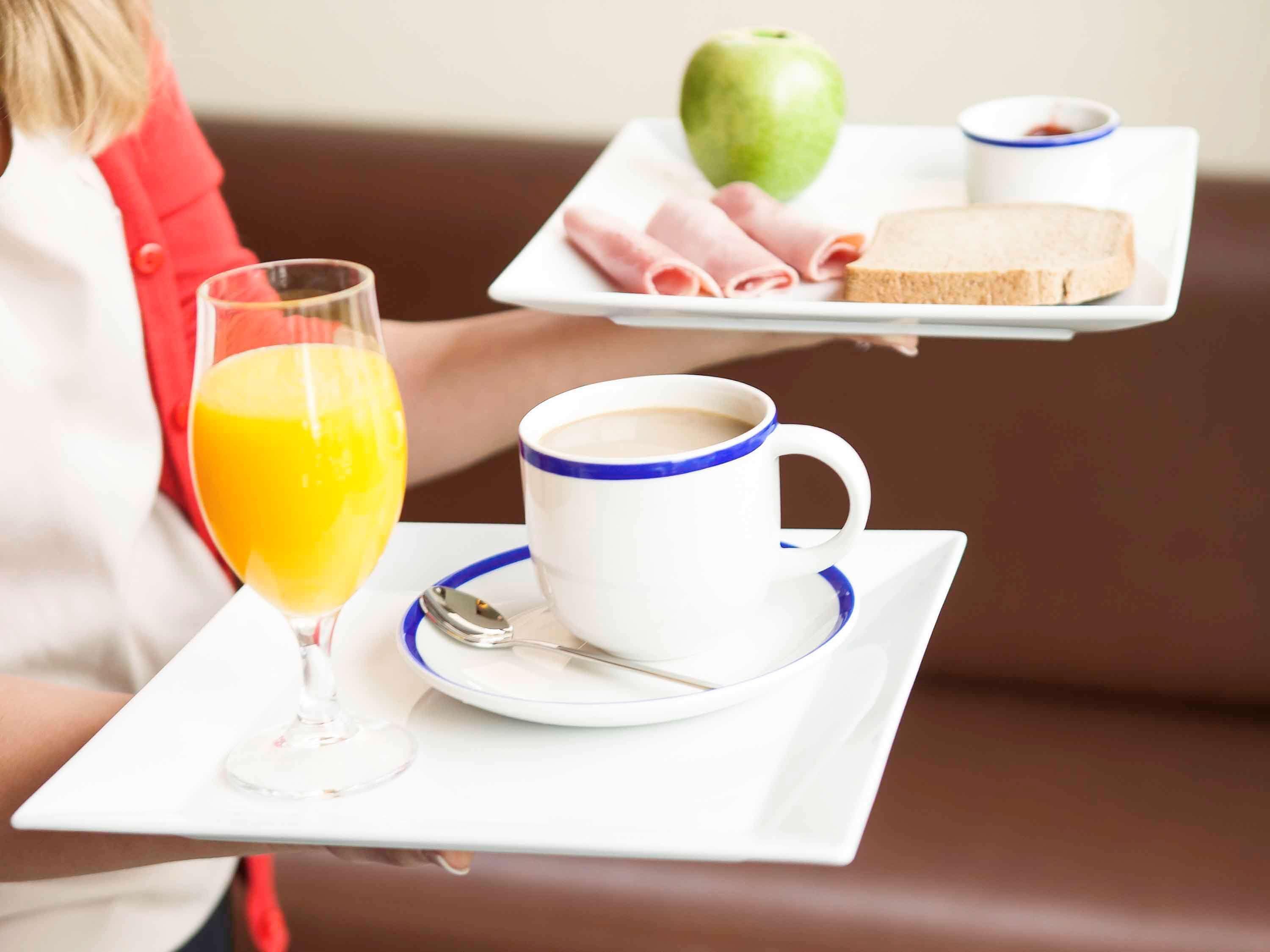 A tray with a glass of orange juice, a cup of coffee, a slice of bread, a piece of ham, and an apple.