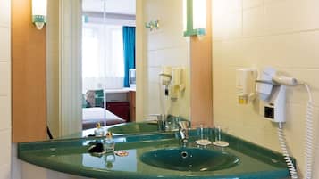 A bathroom with a green glass sink, a mirror, a hairdryer, and a telephone.