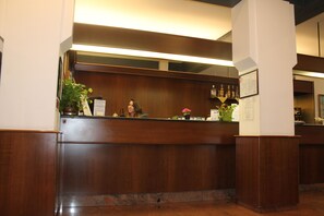 Un mostrador de recepción con detalles de madera, una planta en maceta y un menú enmarcado en la pared.