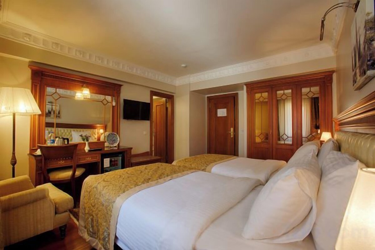 A hotel room with two beds, a desk with a chair, a mirror, and a television.