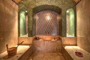 A traditional bath area with a marble floor, a wooden basin, and a decorative tiled wall.