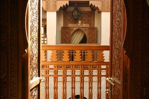 An ornate wooden gate with intricate carvings, leading to a room with a patterned wall and a decorative lamp. - Riad Kniza (Marrakech)