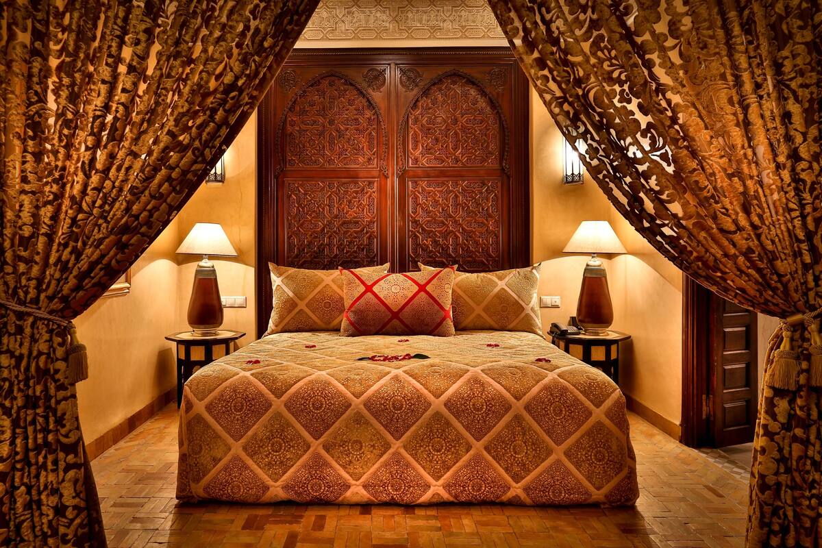 A traditional room with a large bed, ornate wooden door, and patterned curtains.