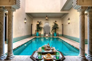 A pool area with a tray of food and drinks, surrounded by marble columns and decorative lighting.