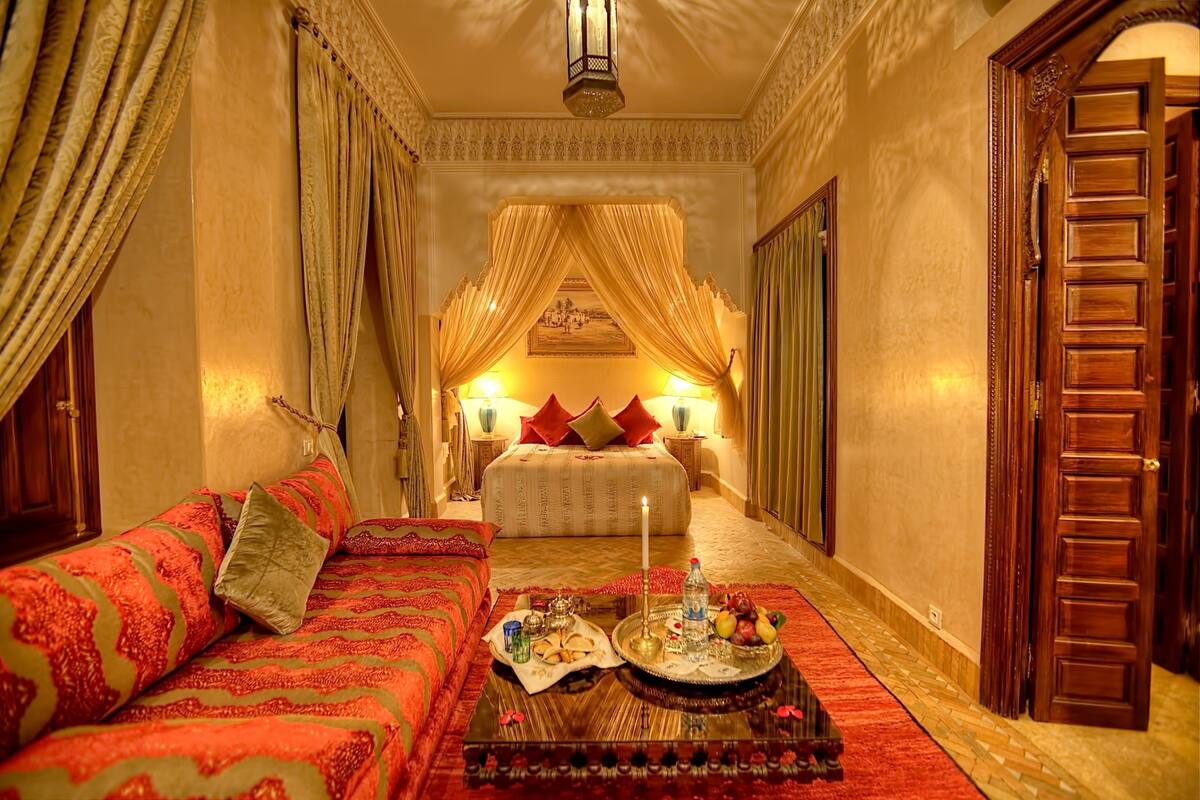 A luxurious bedroom with a bed, a sofa, a tray with items, and a chandelier.