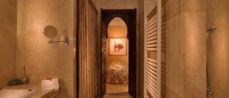 A narrow hallway with a bathroom on the left, a bed in the center, and a shower on the right.