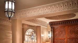 Un intérieur marocain traditionnel, avec des boiseries richement décorées, un ensemble de canapés moelleux, une table basse sur laquelle sont disposés des fruits et un lustre.