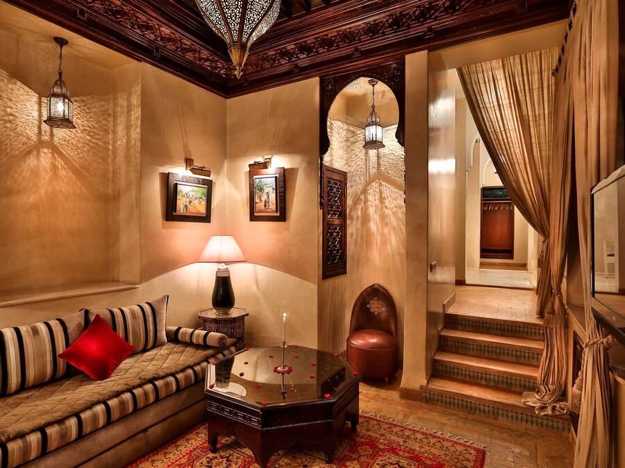 A cozy living room with a sofa, a coffee table, and a lamp. There are framed pictures on the wall and a staircase leading to another room.