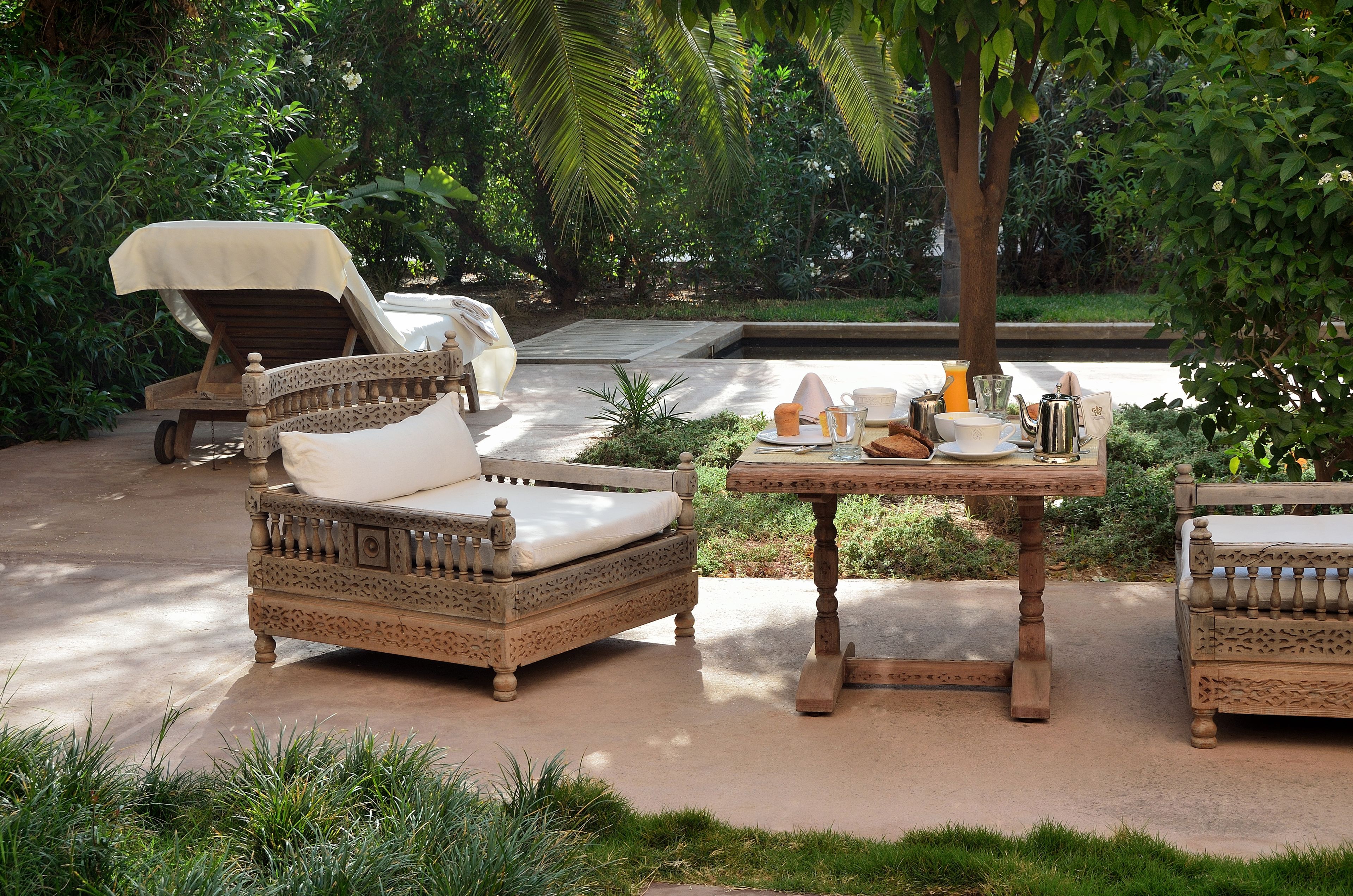A garden patio with wicker furniture, a table with various items, and lush greenery.