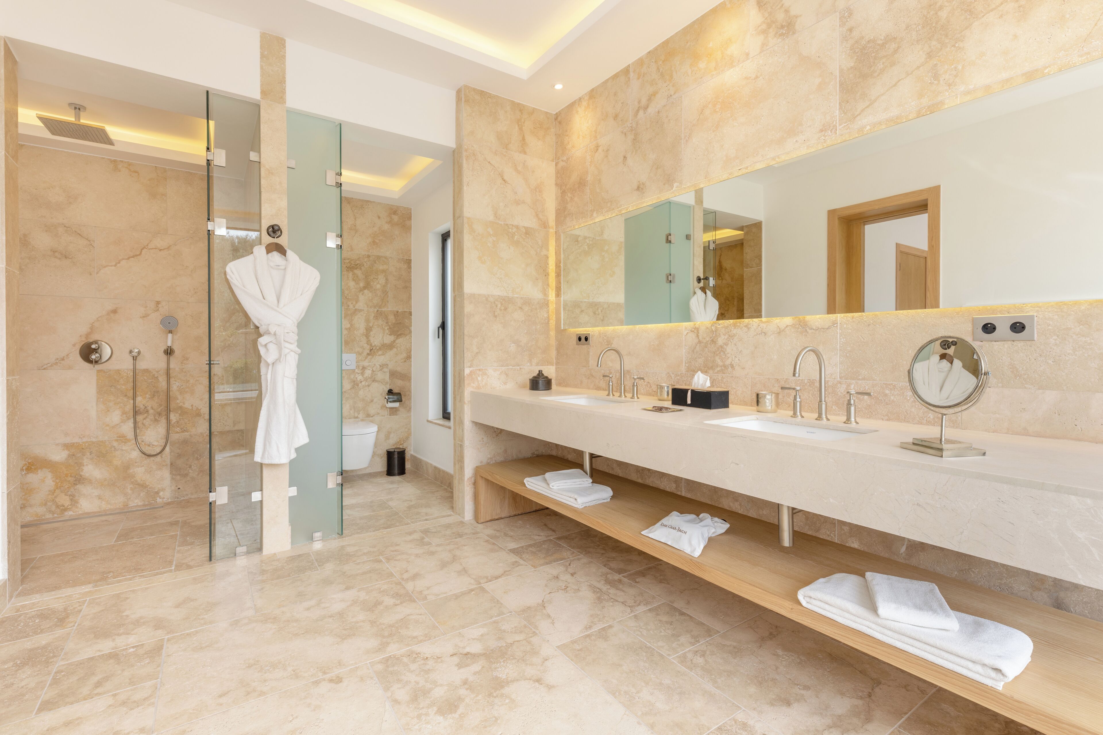 A modern bathroom with a glass-enclosed shower, a vanity with a large mirror, and neatly folded towels on a shelf.