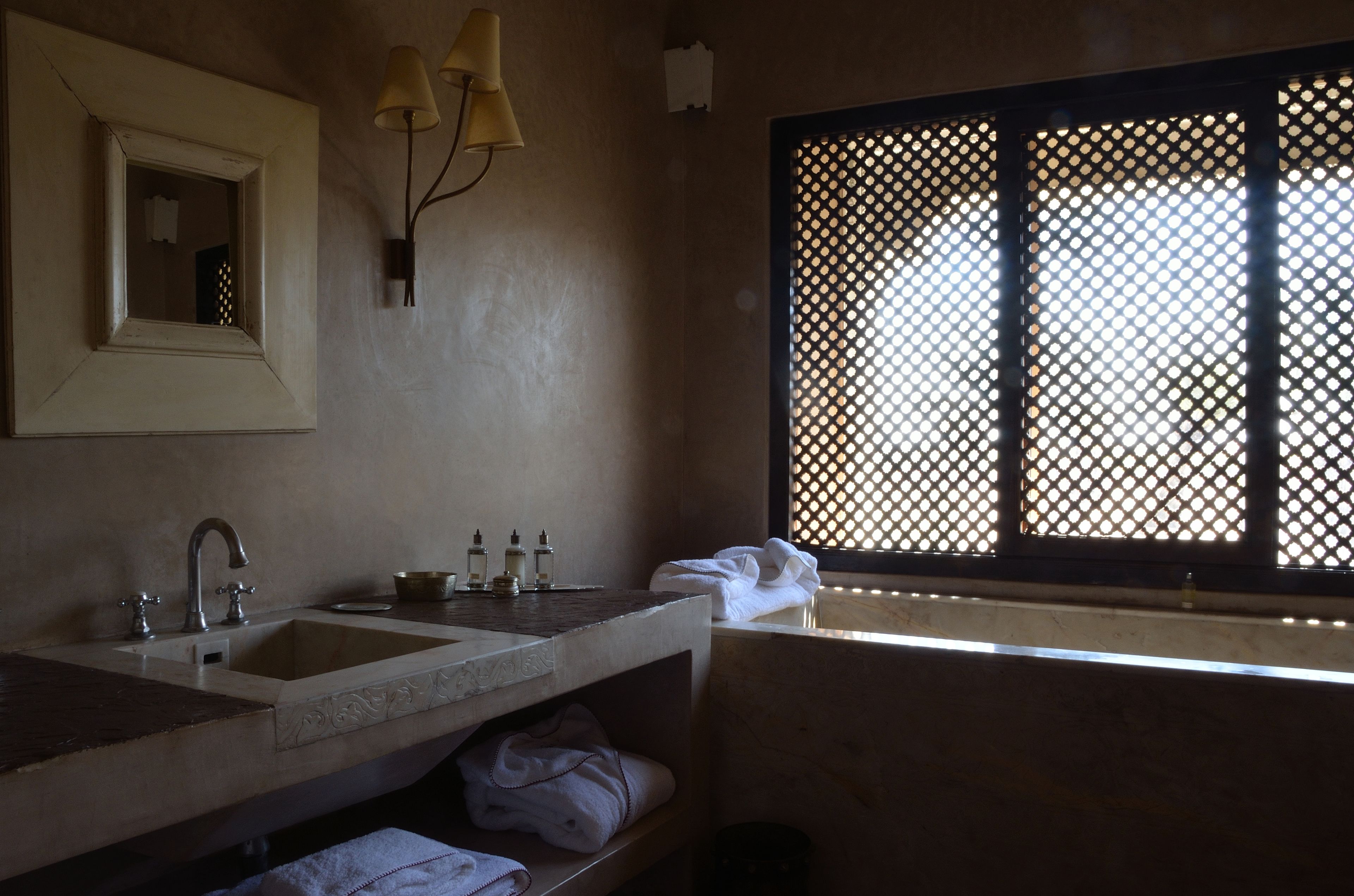 A bathroom with a large sink, mirror, and window with a lattice design.