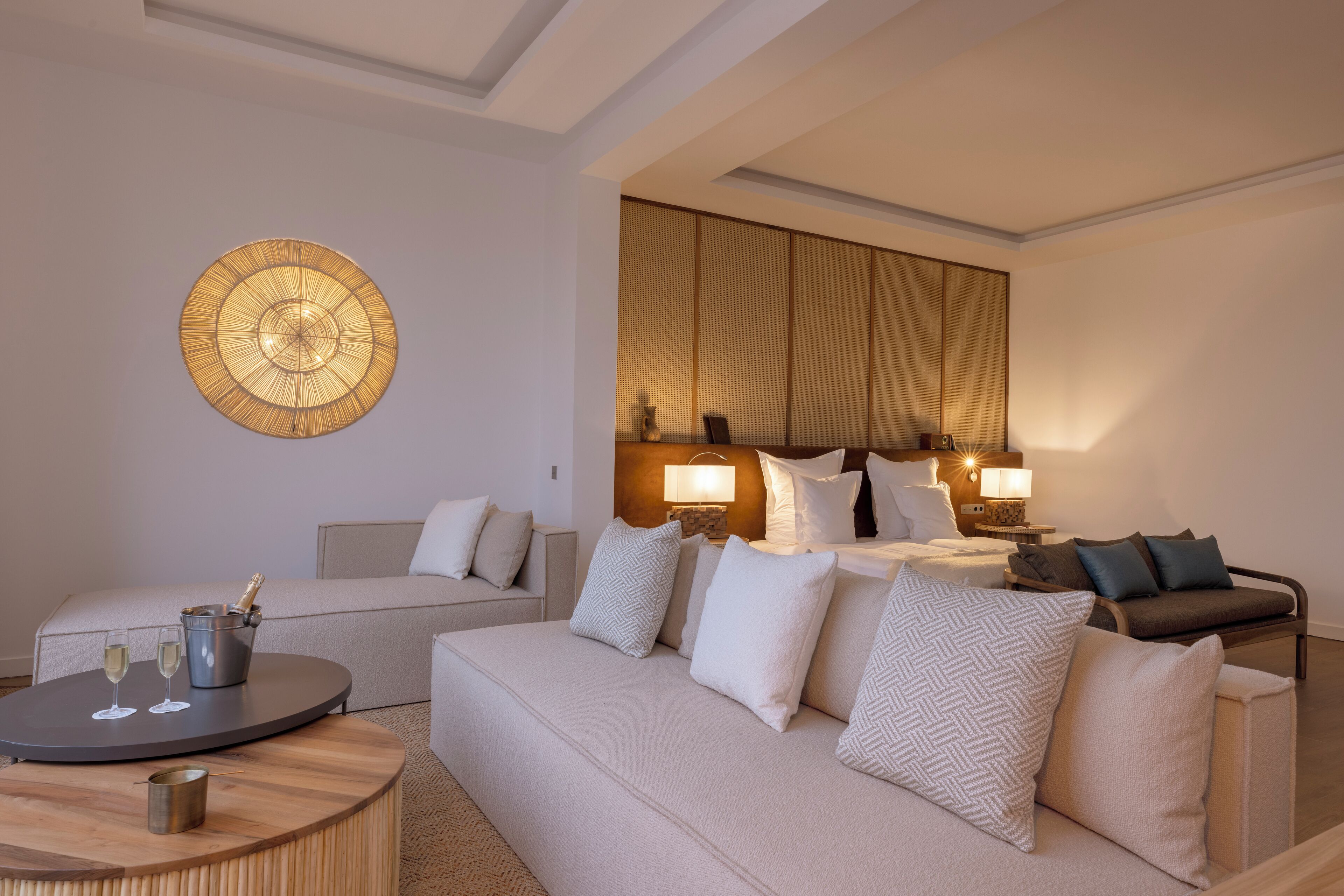 Une chambre d’hôtel moderne avec un grand canapé, une table basse ronde et une lampe fixée au mur.