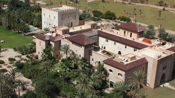 An aerial view of a large, historic building with multiple towers and a courtyard surrounded by palm trees.