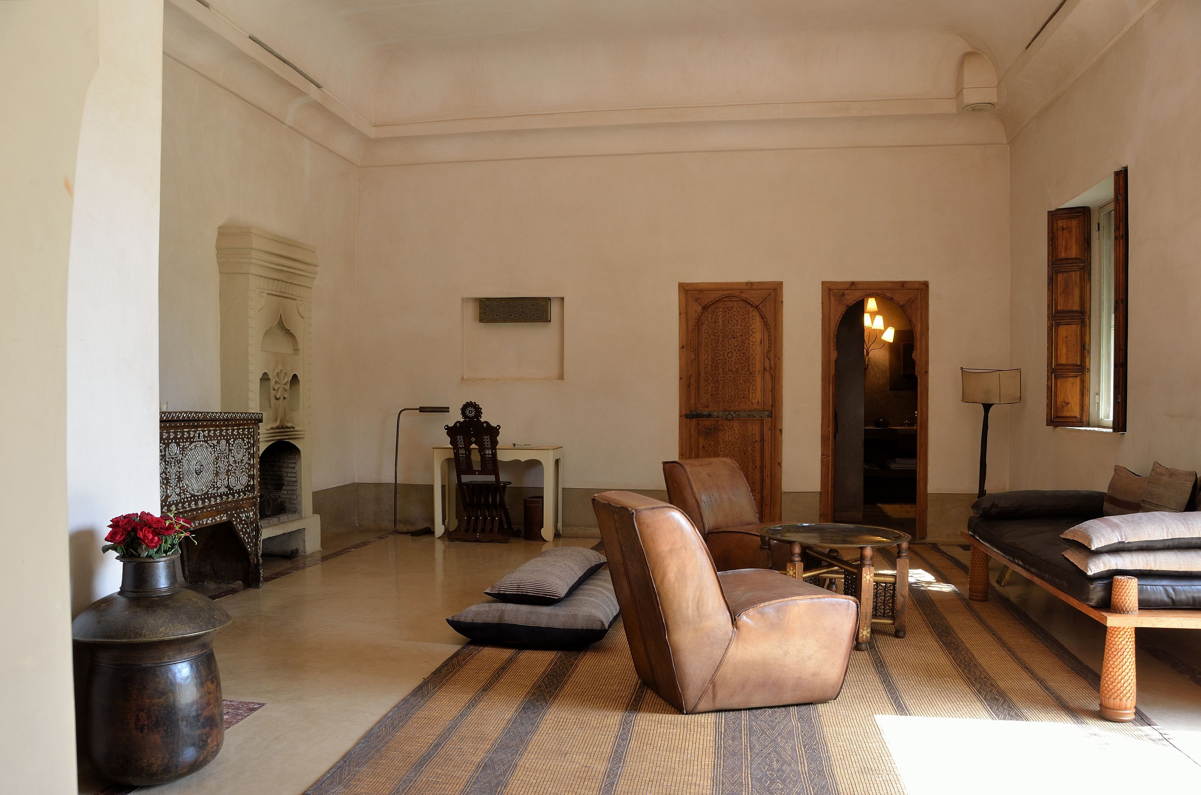 A spacious living room with a sofa, armchairs, and a coffee table. There is a fireplace, a wooden door, and a lamp.