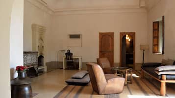 A spacious living room with a sofa, armchairs, and a coffee table. There is a fireplace, a wooden door, and a lamp.