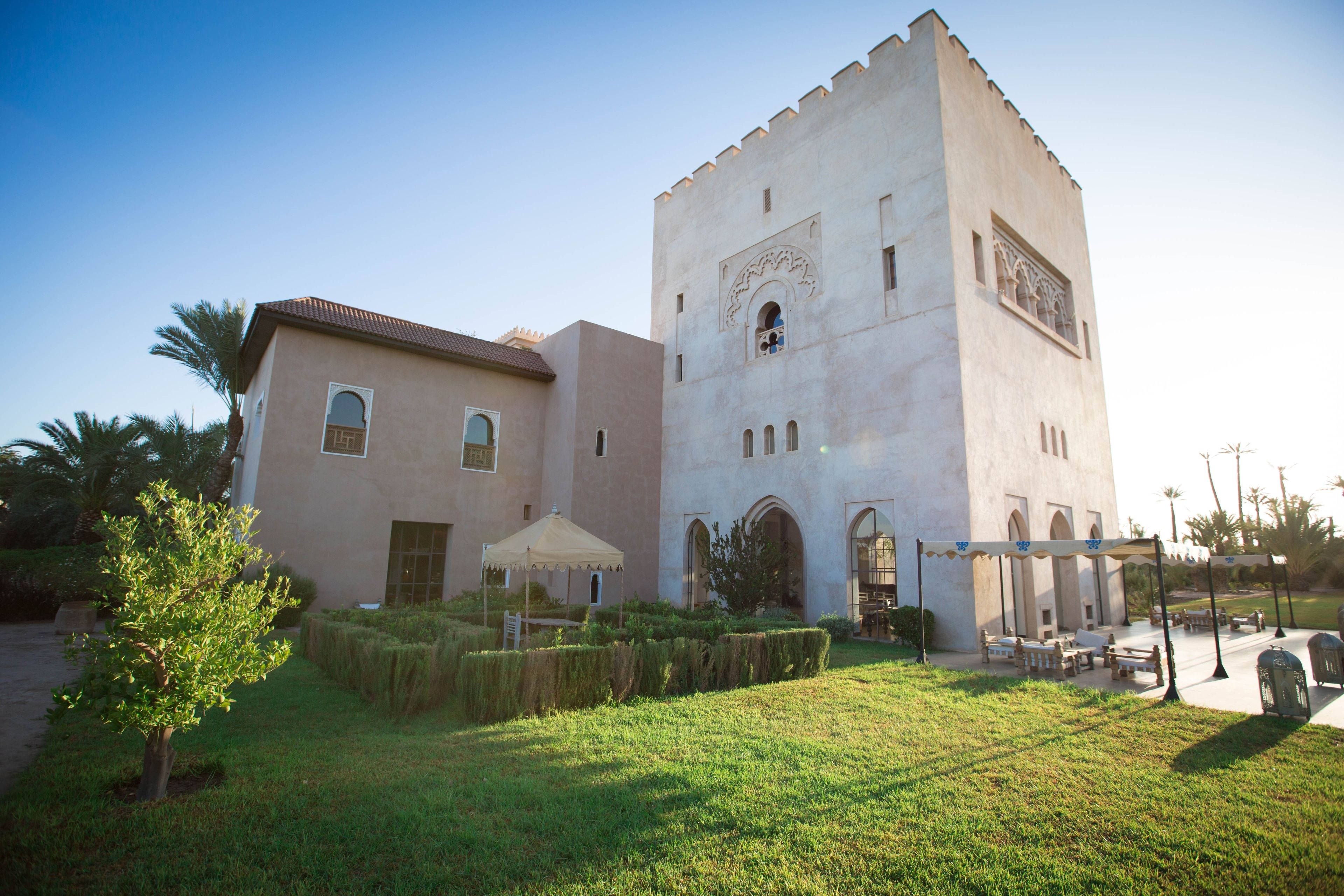 A building with a tower, a covered patio, and a well-maintained garden.