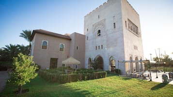A building with a tower, a covered patio, and a well-maintained garden.