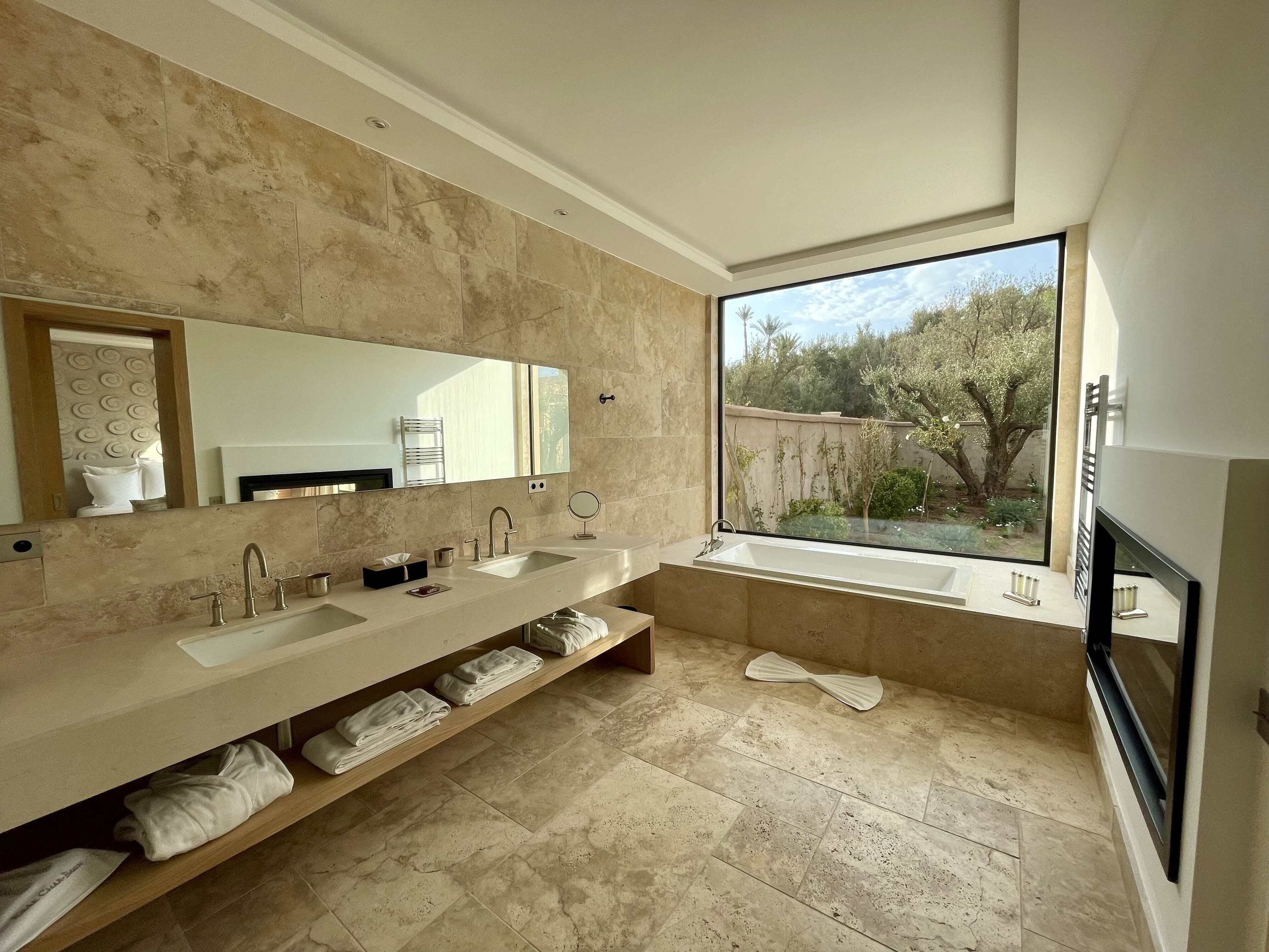 A modern bathroom with two sinks, a large mirror, and a view of a garden through a window.