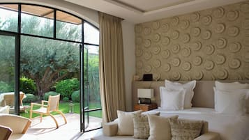 Un dormitorio con una cama grande, un sofá y una silla. Se ve vegetación a través de la ventana.