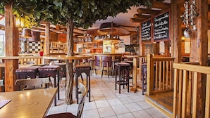Un restaurante acogedor con mobiliario de madera, un árbol central y una pizarra con el menú.