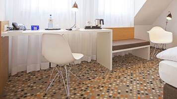 A hotel room with a bed, a desk with a chair, a small seating area, and a patterned floor.