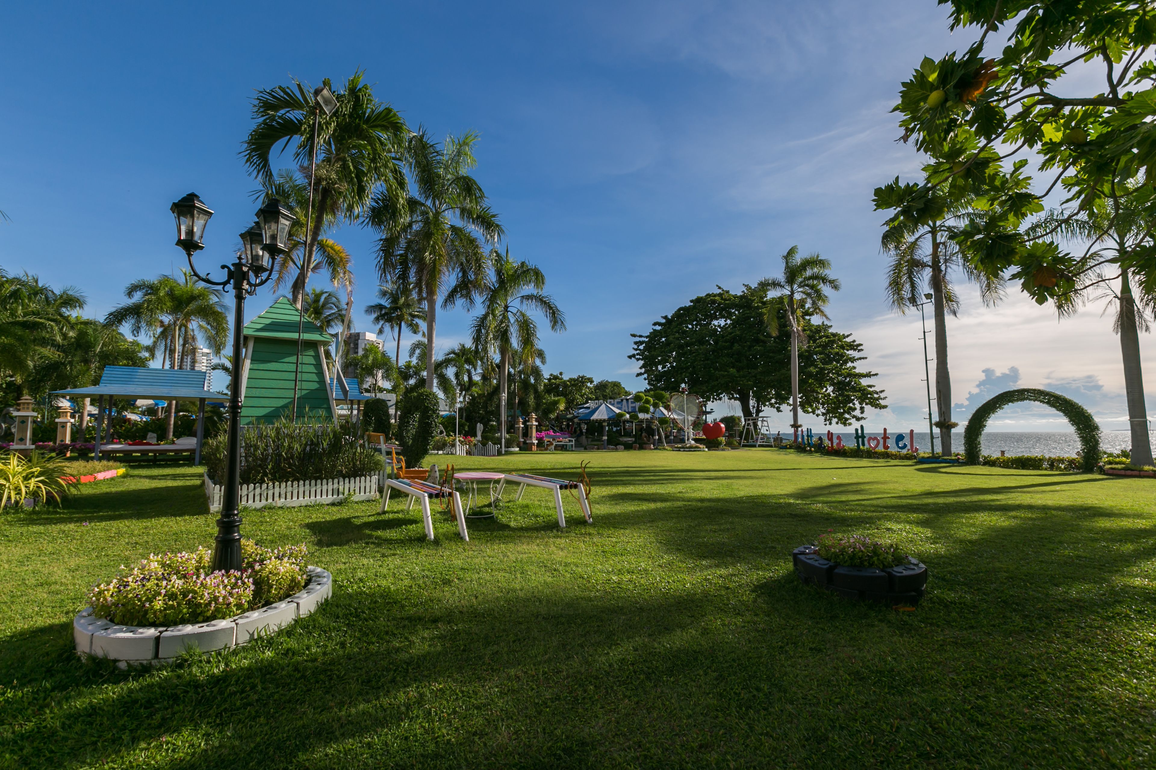 A well-maintained garden with palm trees, a gazebo, and a clear view of the sea.
