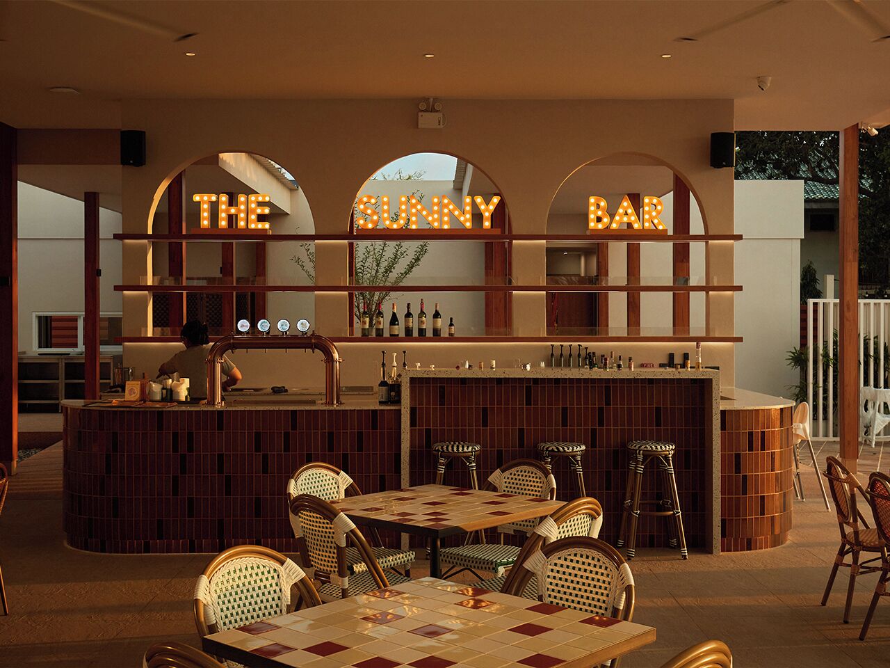 Una zona de bar con pared de azulejos, muebles de madera y un letrero que dice “THE SUNNY BAR”.