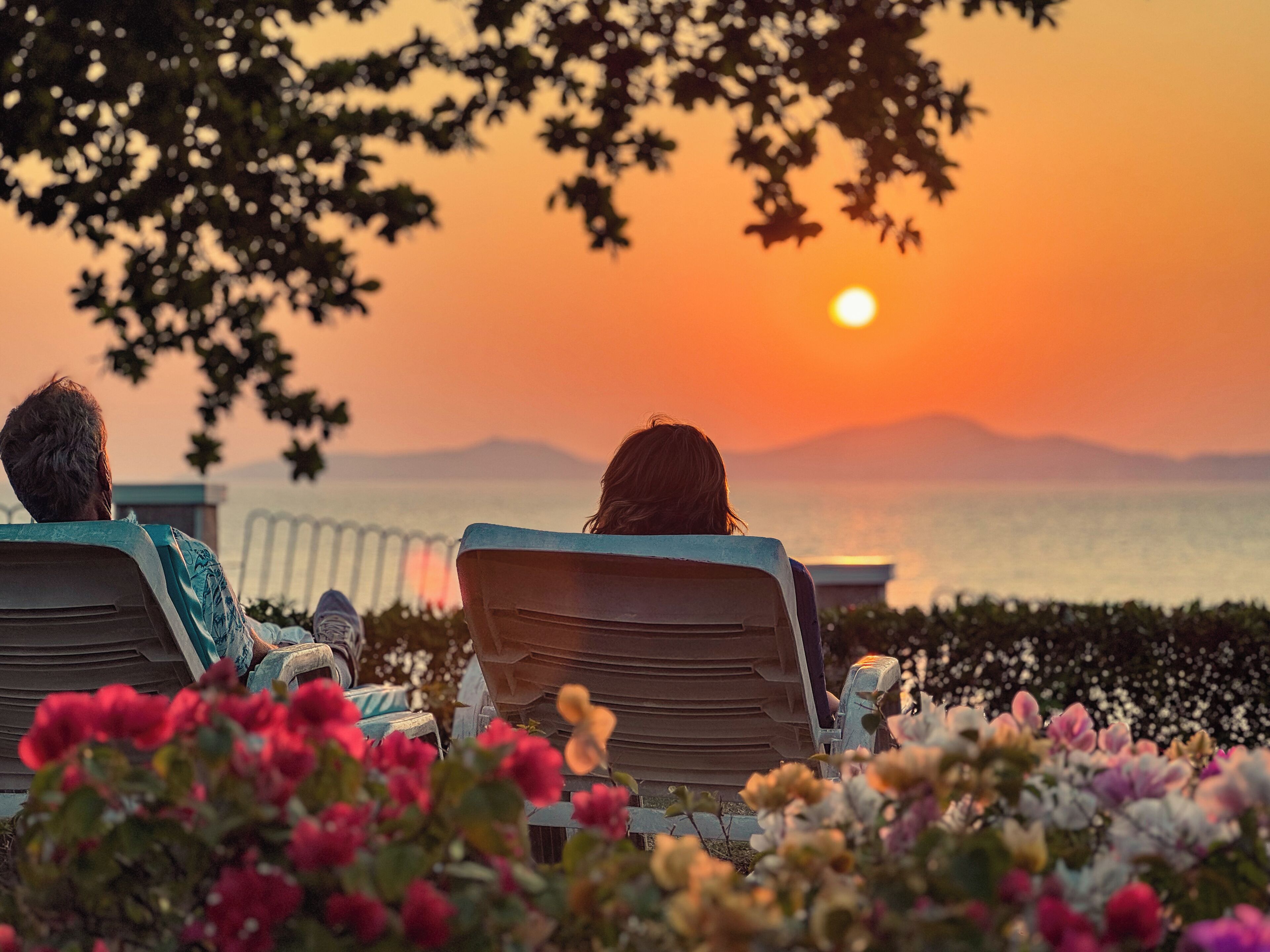 Deux personnes se détendent sur des chaises longues, face à un coucher de soleil sur une étendue d’eau.