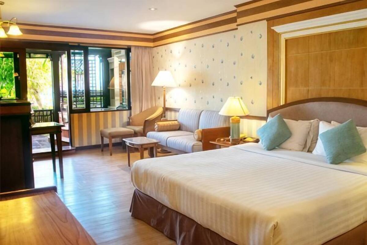 A hotel room with a large bed, two bedside tables, a sofa, a chair, and a small table.
