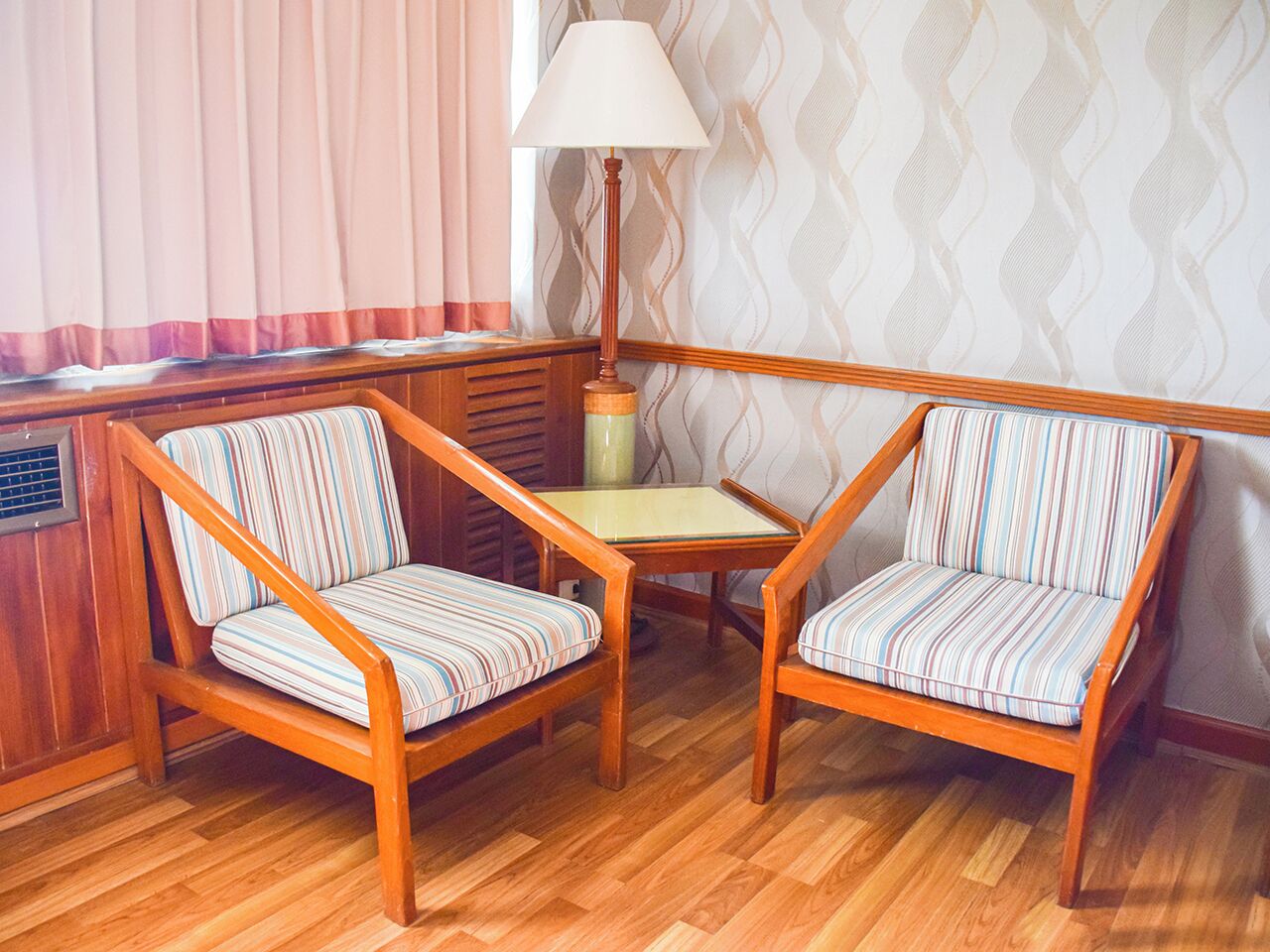 A corner seating area with two striped armchairs and a small table, wooden floor, and a lamp.