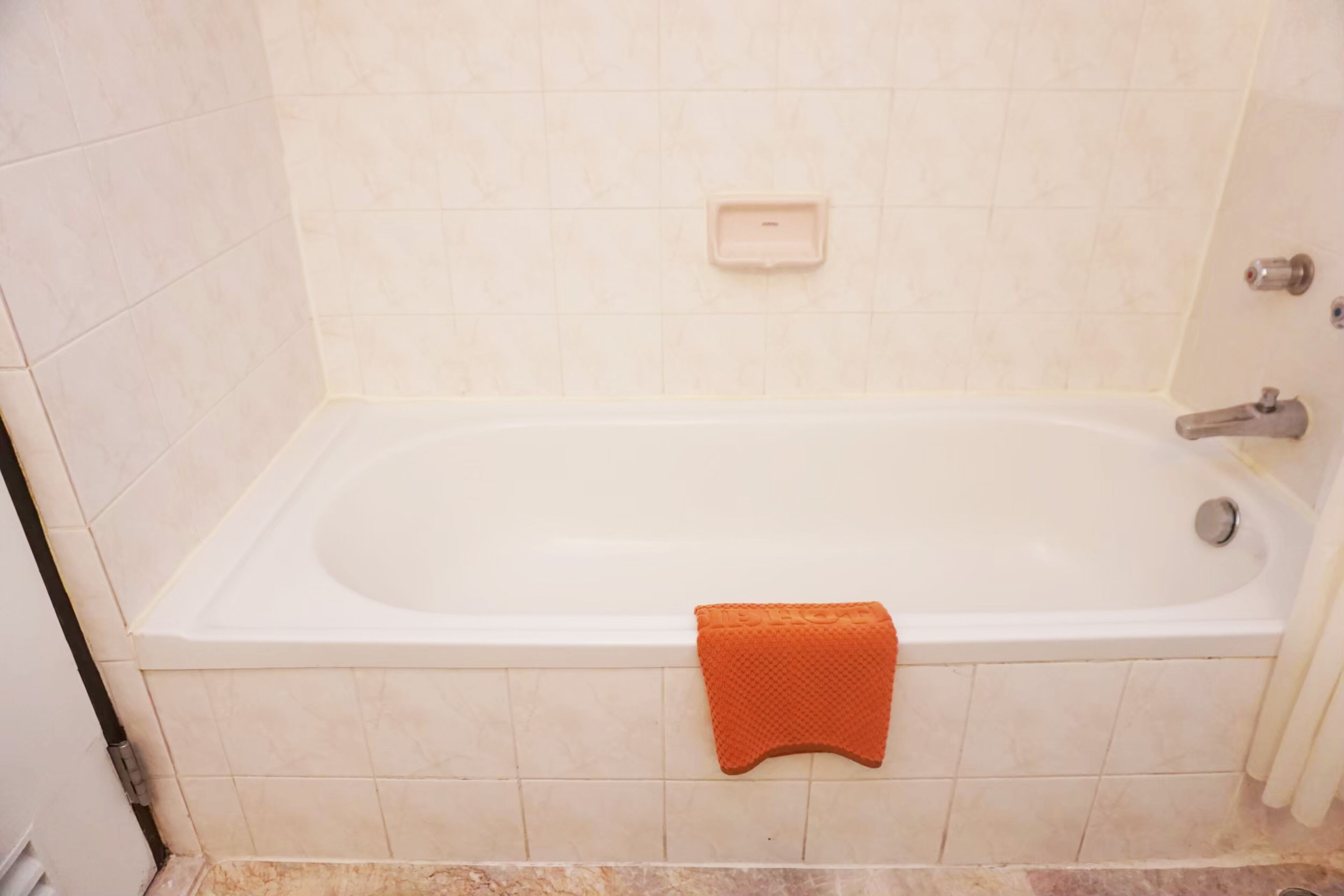 A standard bathtub with a built-in soap dish and a towel rack with a towel.