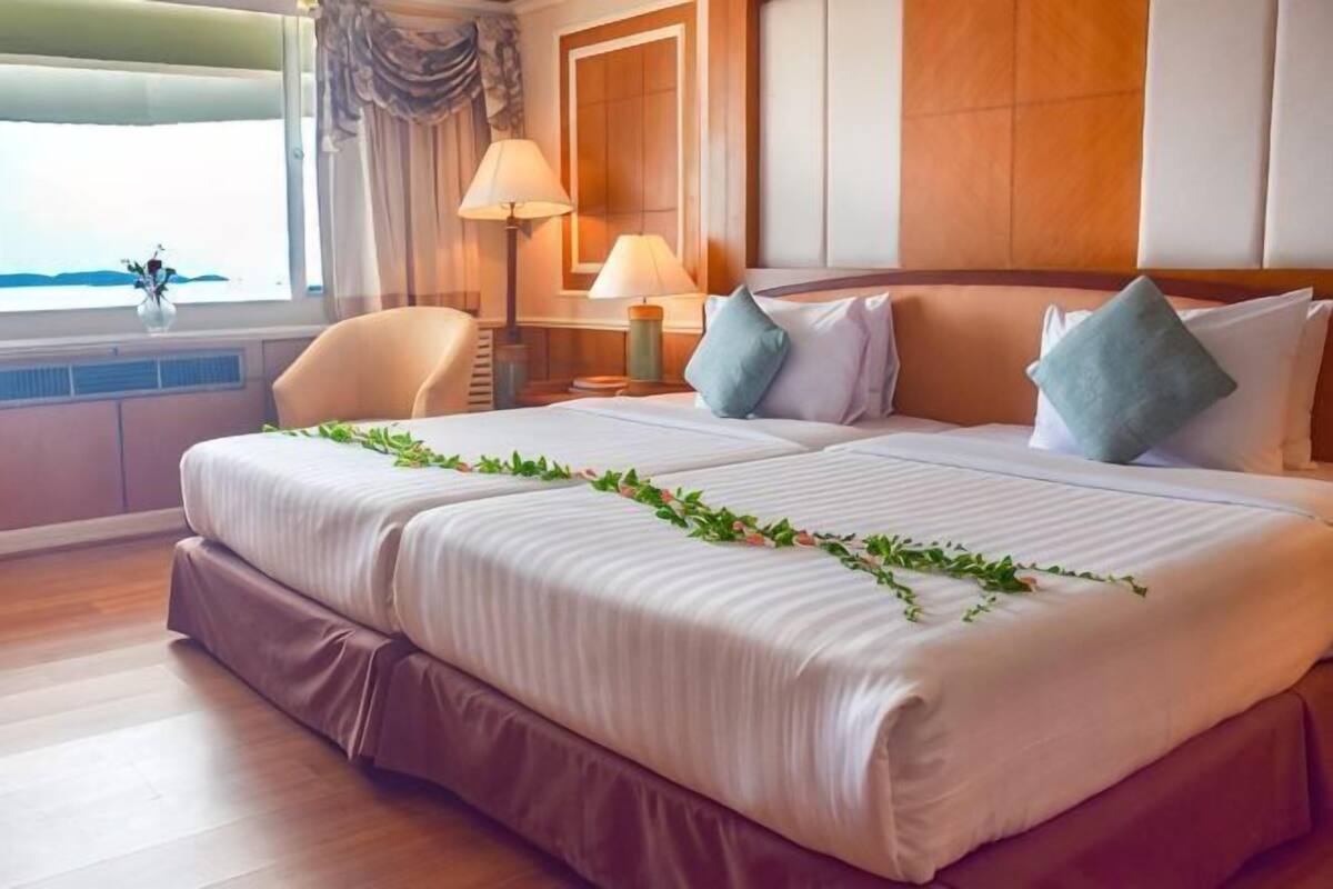 A double bed with a garland, a nightstand with a lamp, a chair, and a window with curtains.