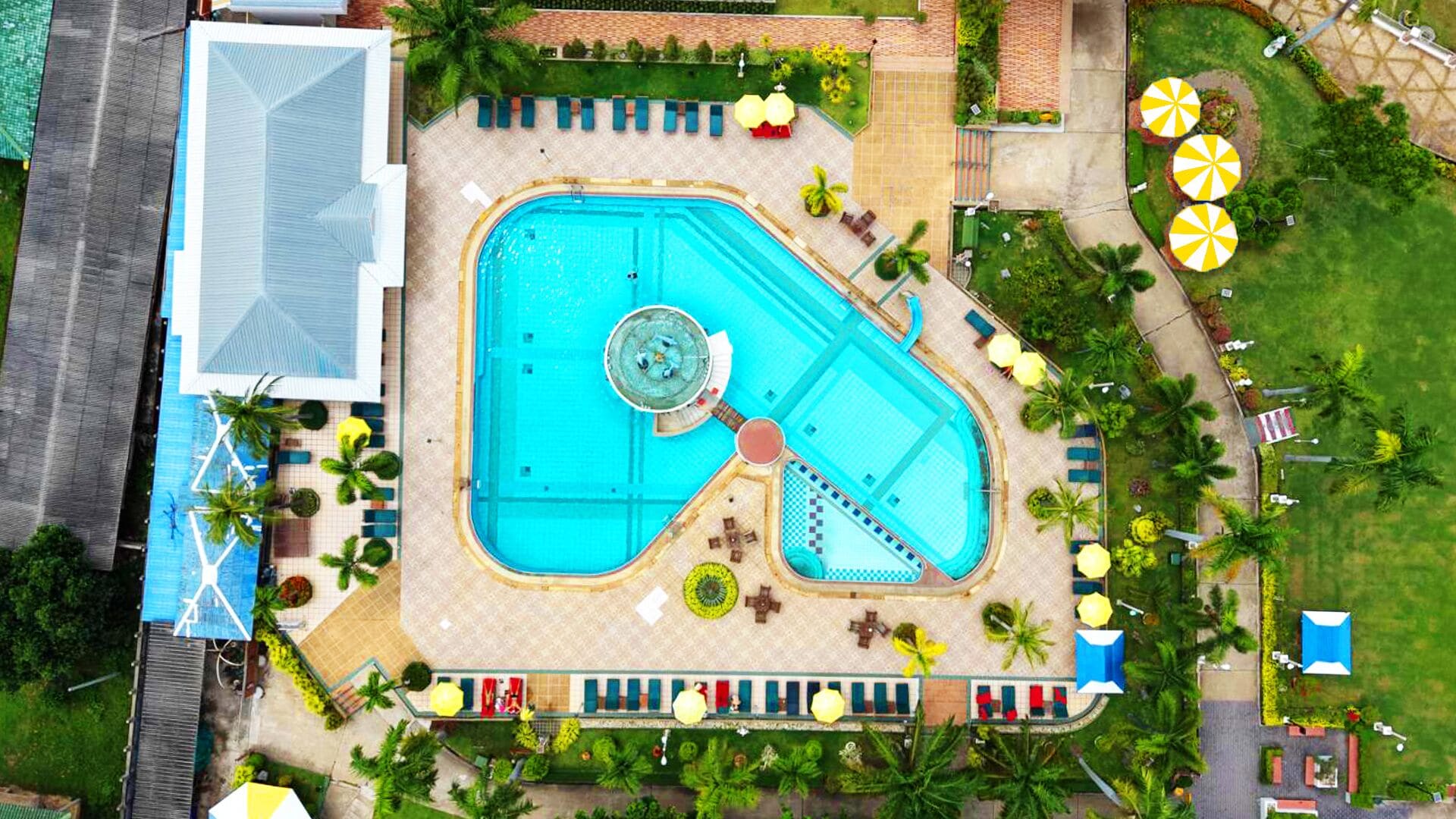 An aerial view of a hotel with a large swimming pool, sun loungers, and palm trees.