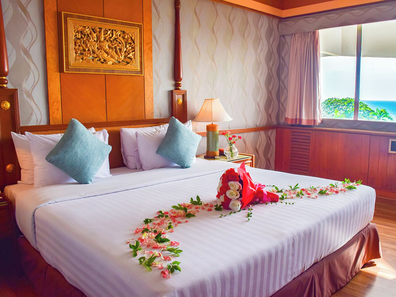 A neatly made bed with white linens, blue and white pillows, and a floral arrangement on the bed.