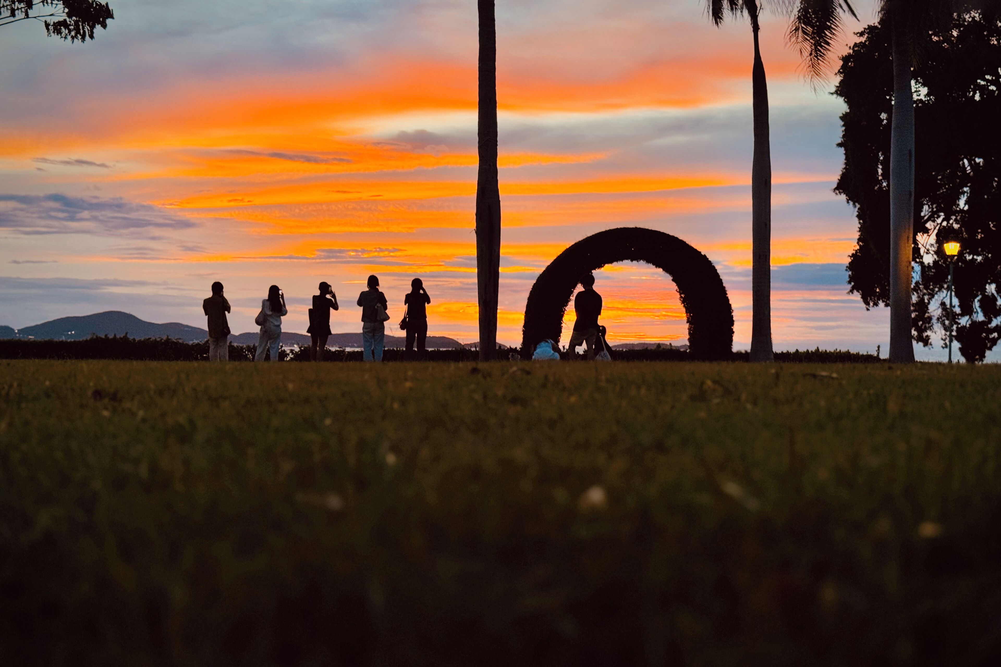 Un coucher de soleil avec les silhouettes de personnes et une structure circulaire dans un champ herbeux.