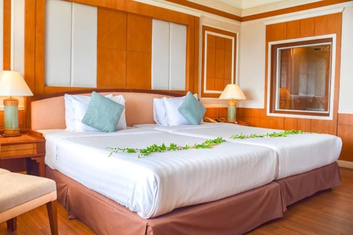 A hotel room with a large bed, wooden paneling, two bedside tables with lamps, and a window.