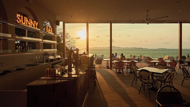 A modern bar with a view of the sea, featuring a bar counter, seating area, and large windows. - Asia Pattaya Hotel (Pattaya)