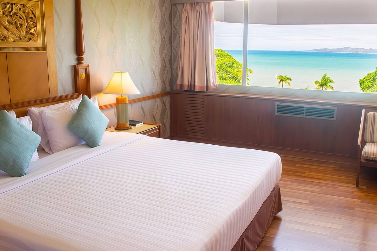 A hotel room with a large bed, a chair, a nightstand, a lamp, and a view of the beach.