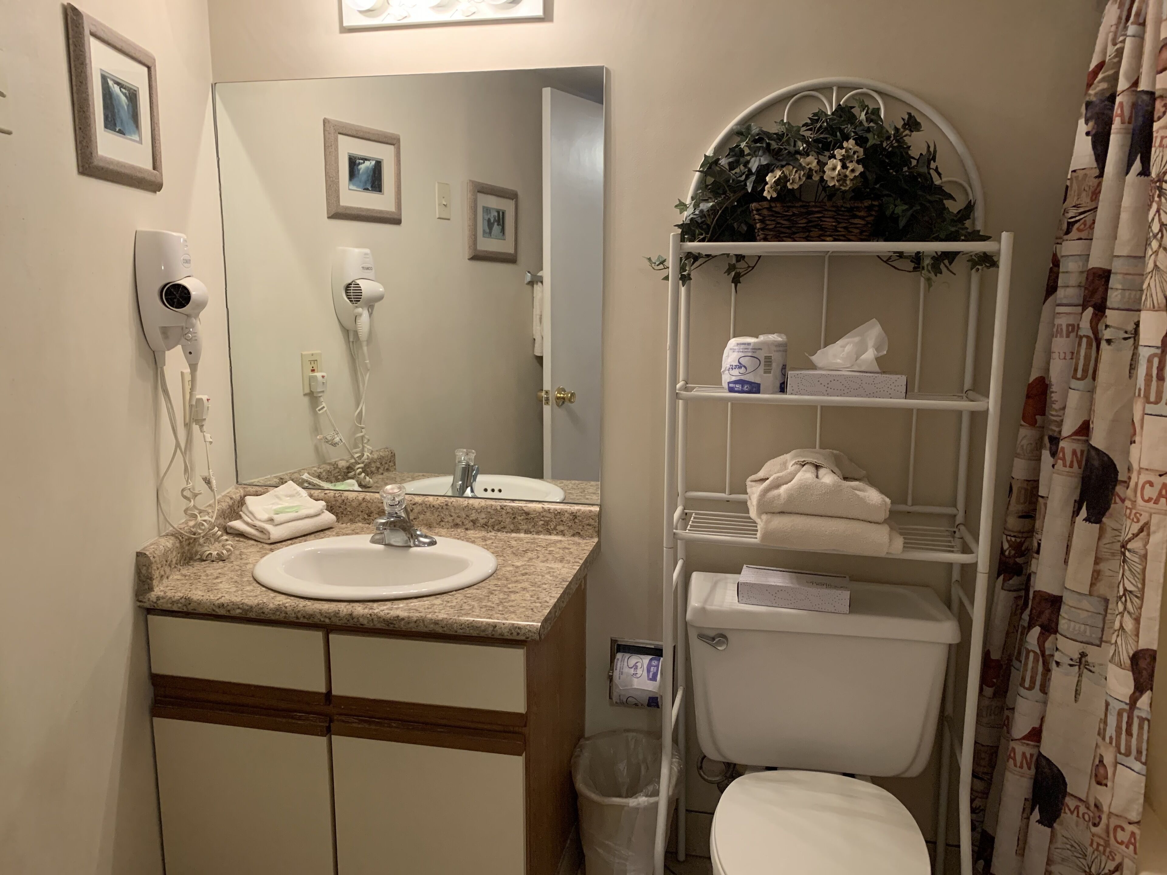 Casa de banho com lavatório, espelho, secador de cabelo e prateleiras com produtos de higiene pessoal.