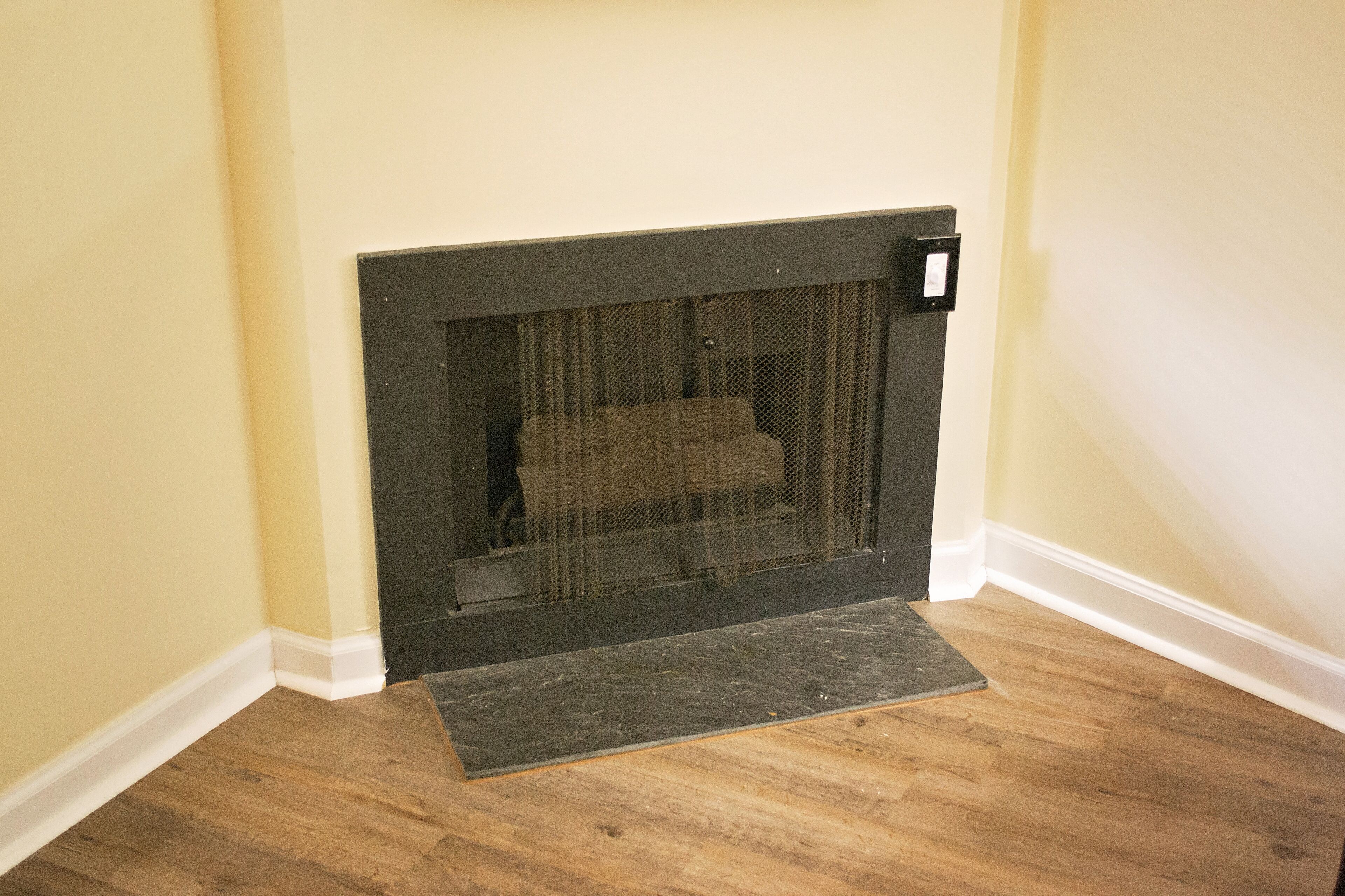 A corner fireplace with a screen, a small step, and a wall-mounted control panel.