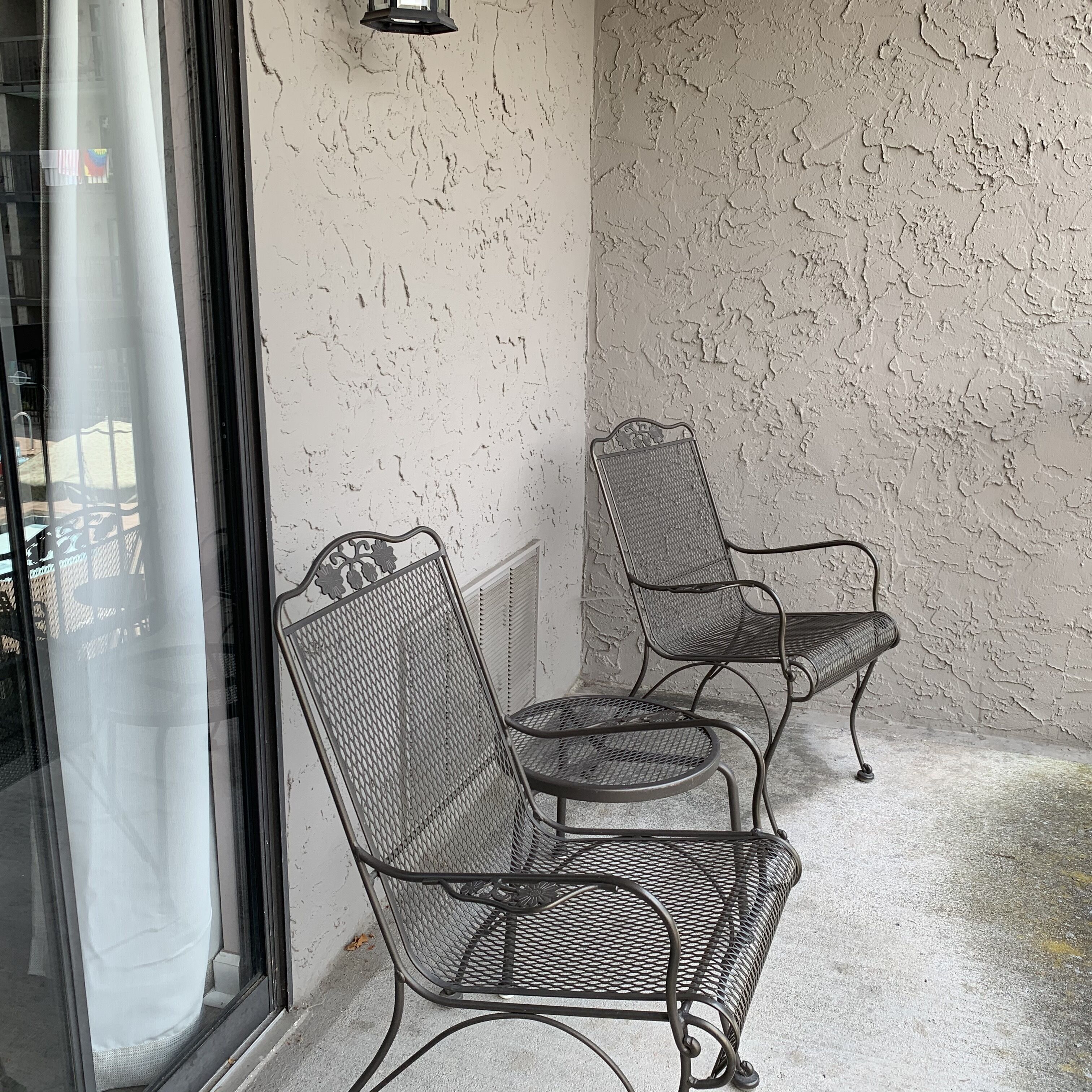 Zwei Stühle mit Netzbespannung an Rückenlehne und Sitzfläche, vor einer strukturierten Wand, links ist ein Fenster zu sehen.