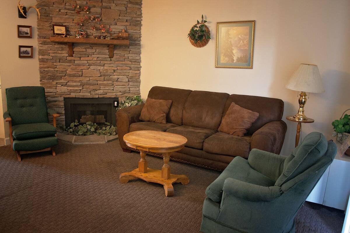 A cozy living room with a stone fireplace, a brown sofa, and two green armchairs.