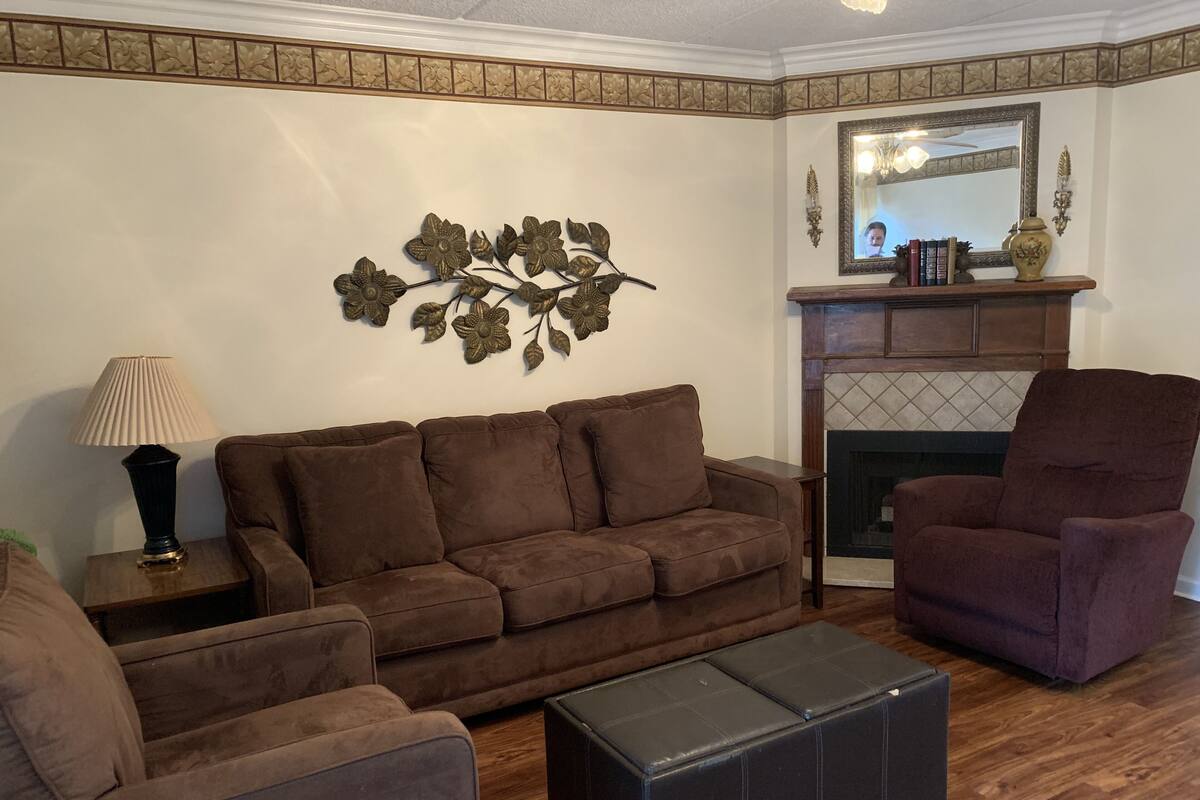 A living room with a brown sofa, a black ottoman, a purple armchair, a lamp, and a fireplace.