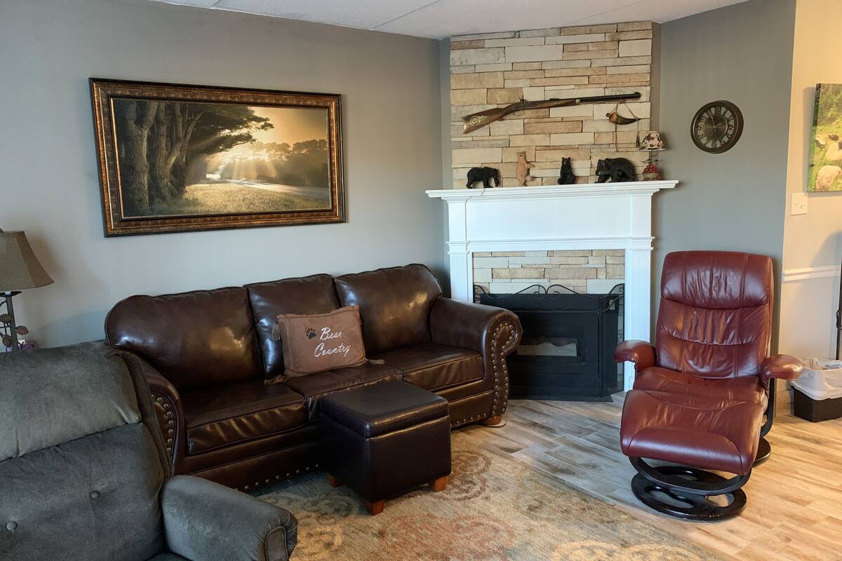 A living room with a brown leather sofa, a brown leather armchair, a fireplace, and a painting on the wall.