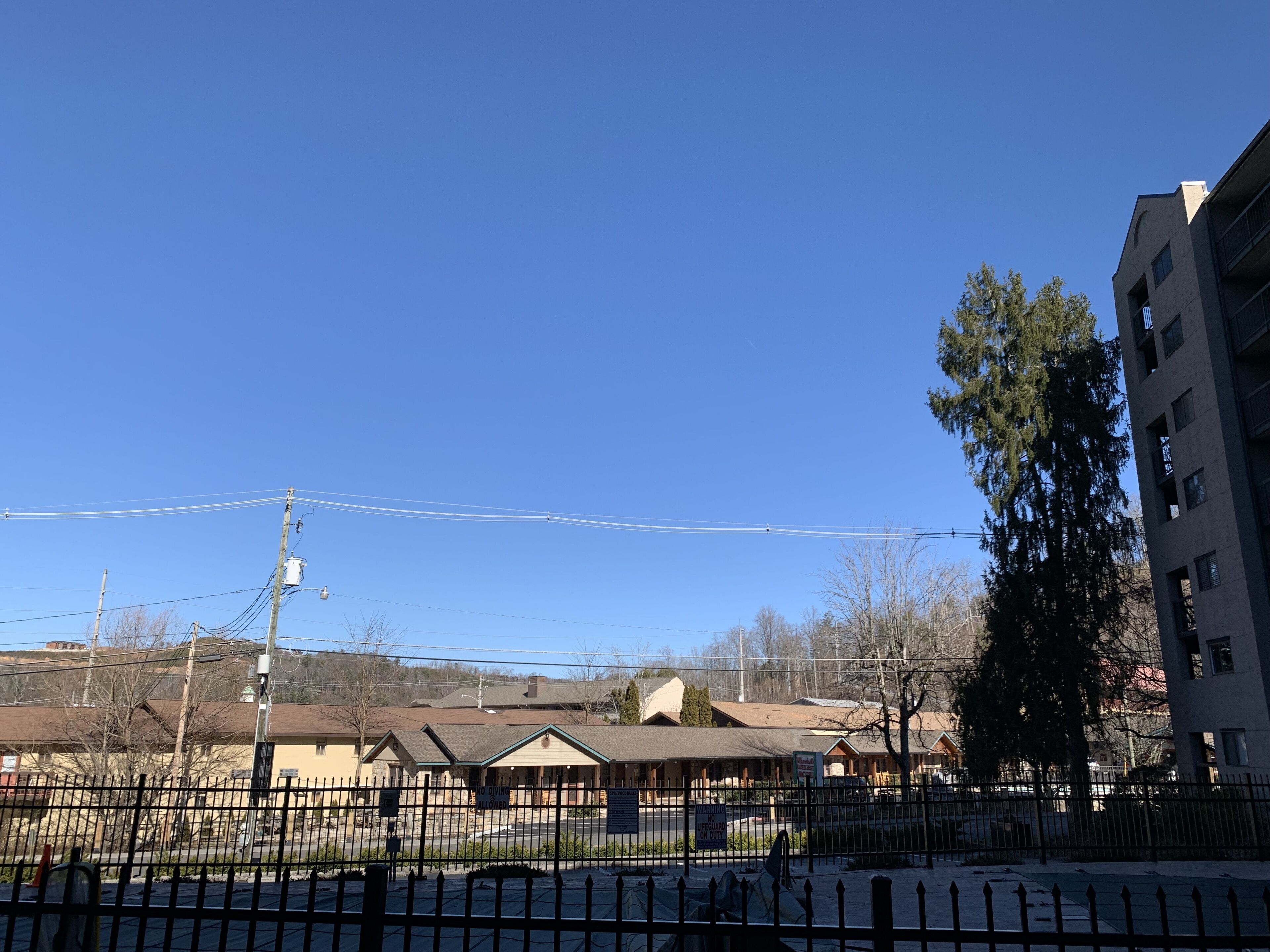 Un espace clos, avec un bâtiment visible à l’arrière-plan, des poteaux électriques et un ciel bleu dégagé.