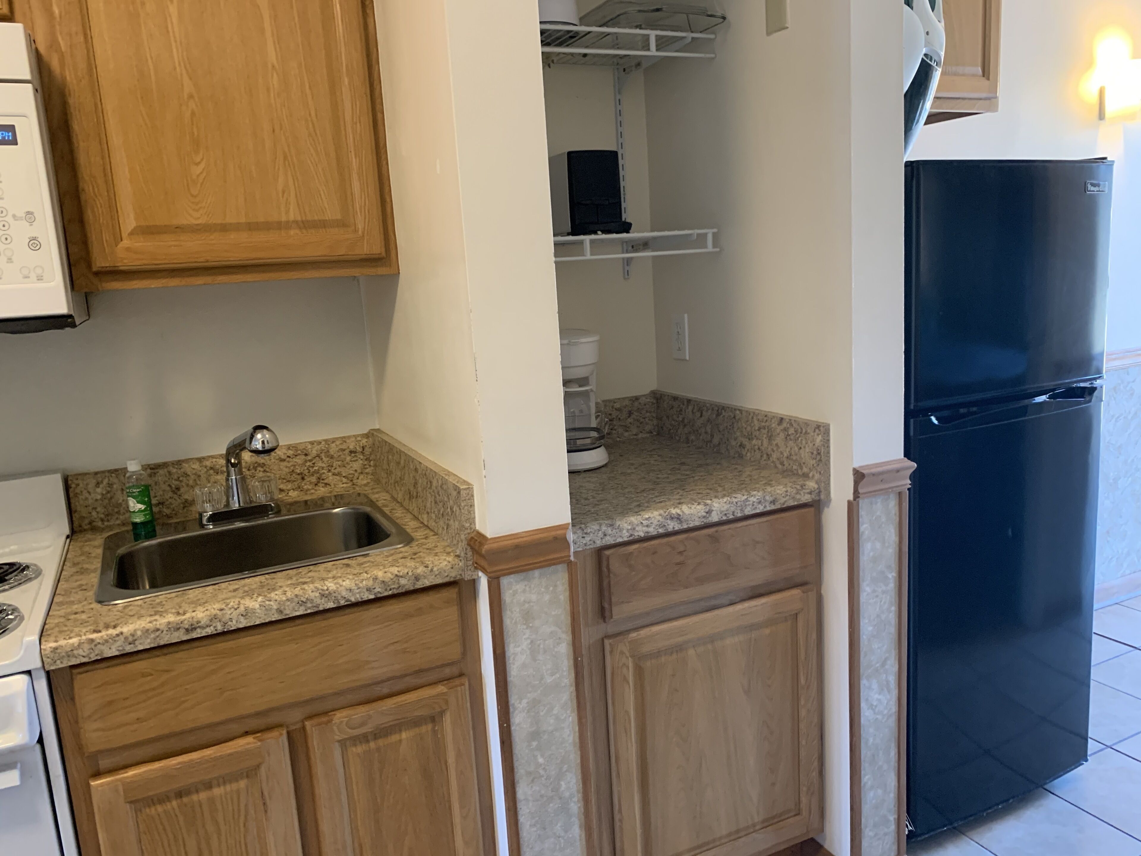 Una cocina con encimeras de granito, armarios de madera, pileta de acero inoxidable, refrigerador negro y cafetera.