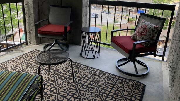 A balcony with two chairs, a small table, and a patterned rug.