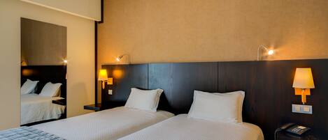Una habitación de hotel con dos camas, un espejo grande, lámparas de noche y un teléfono en la mesita de noche.
