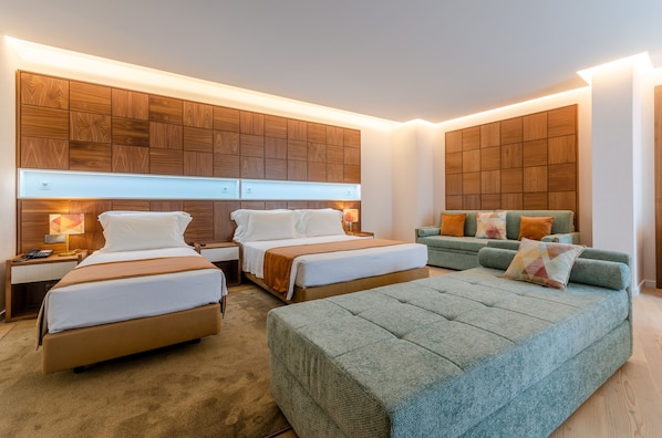 Habitación de hotel con dos camas, un sofá, cabecera de madera panelada y suelo alfombrado.